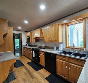 A kitchen with wooden cabinets, a stove, dishwasher, and a window with blinds. - The Serenity Hideaway -3 Bedroom 1 1/2 Bath House (Hinton)