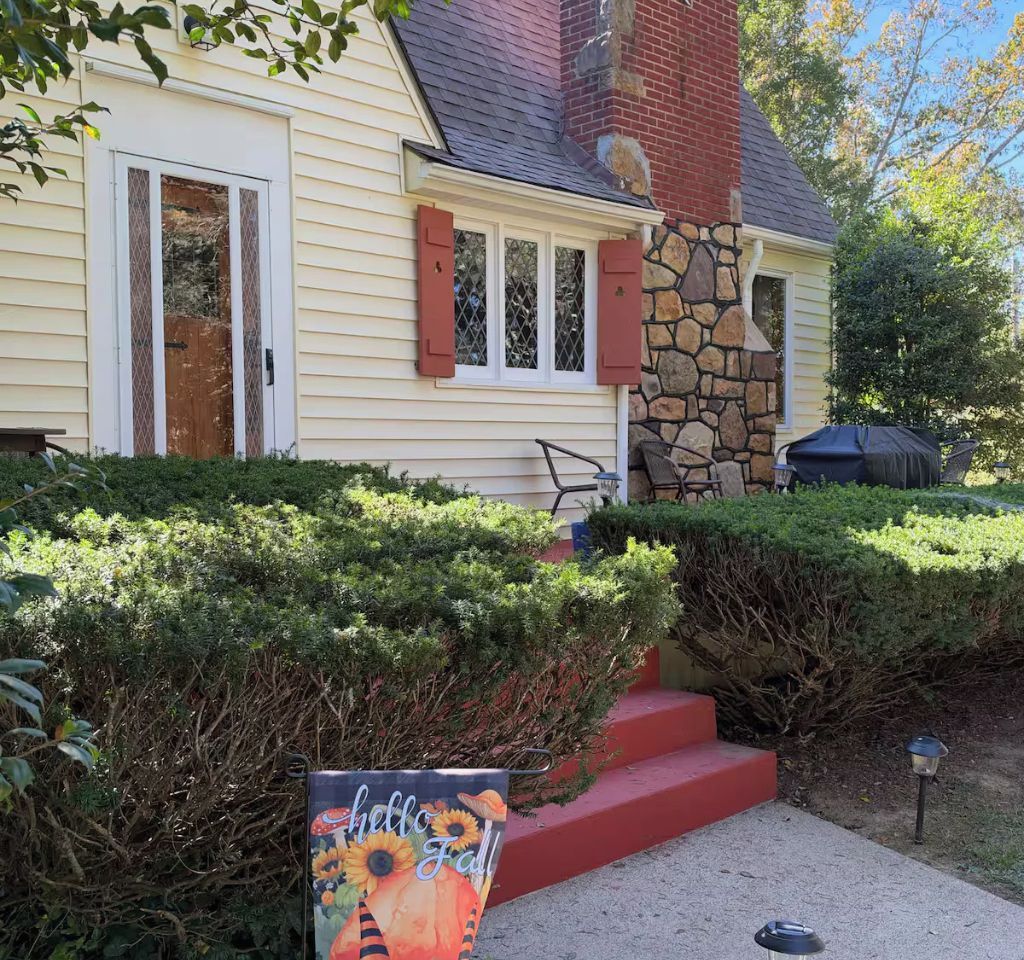 A house with a stone chimney, a covered patio, and a 'hello Fall' sign.
