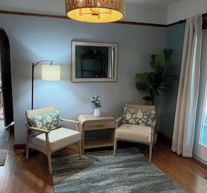 A corner room with two wooden chairs, a small table, a floor lamp, a mirror, and a large plant. - The Serenity Hideaway -3 Bedroom 1 1/2 Bath House (Hinton)
