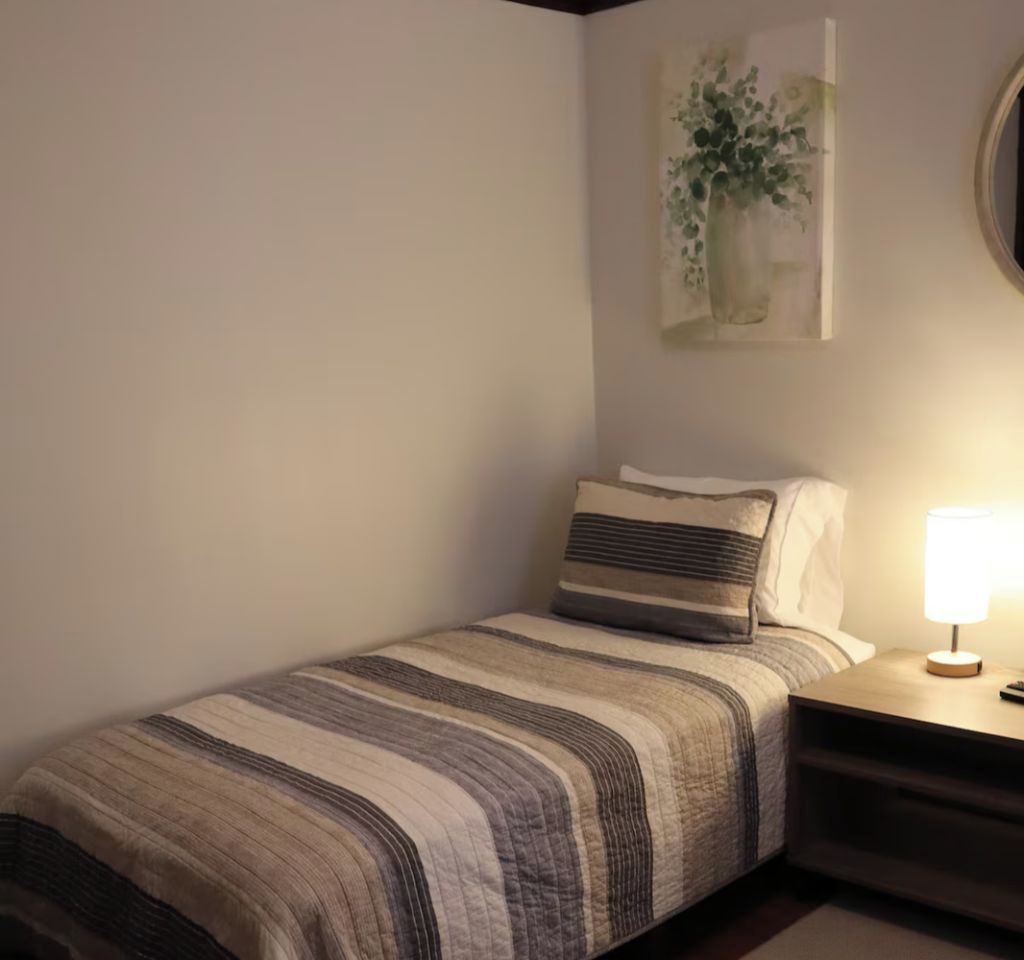 A single bed with a striped bedspread, a bedside lamp, and a wall-mounted painting.