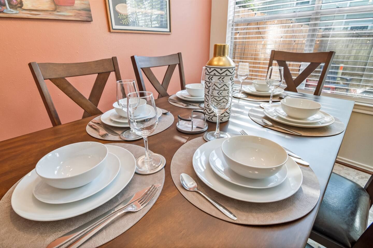 A dining table set with white plates, bowls, and cutlery, with a patterned vase and a bottle on the table.