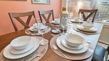 A dining table set with white plates, bowls, and cutlery, with a patterned vase and a bottle on the table.