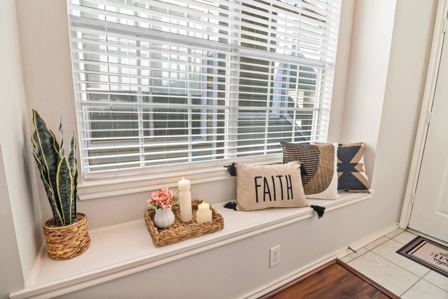 A window seat with a woven basket, candles, and decorative pillows.