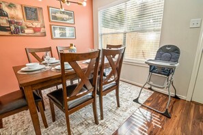 A dining area with a wooden table, chairs, and a high chair. There are framed pictures on the wall and a window with blinds. - House 3-Bed 2,5-Bath FREE Parking - Nice Backyard (Spring)