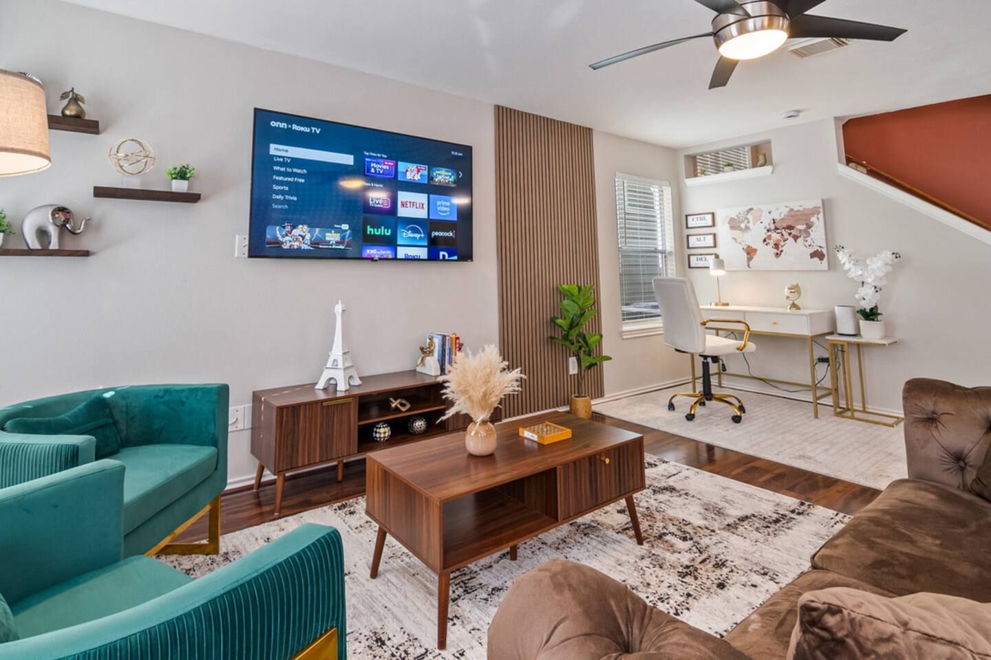 A modern living room with a flat-screen TV, a desk, and two sofas.