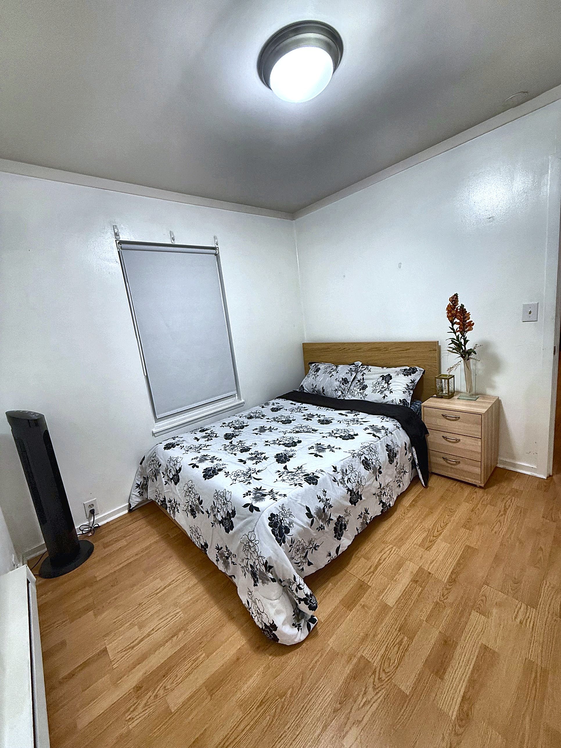 Een slaapkamer met een bed, nachtkastje en een raam met jaloezieën.