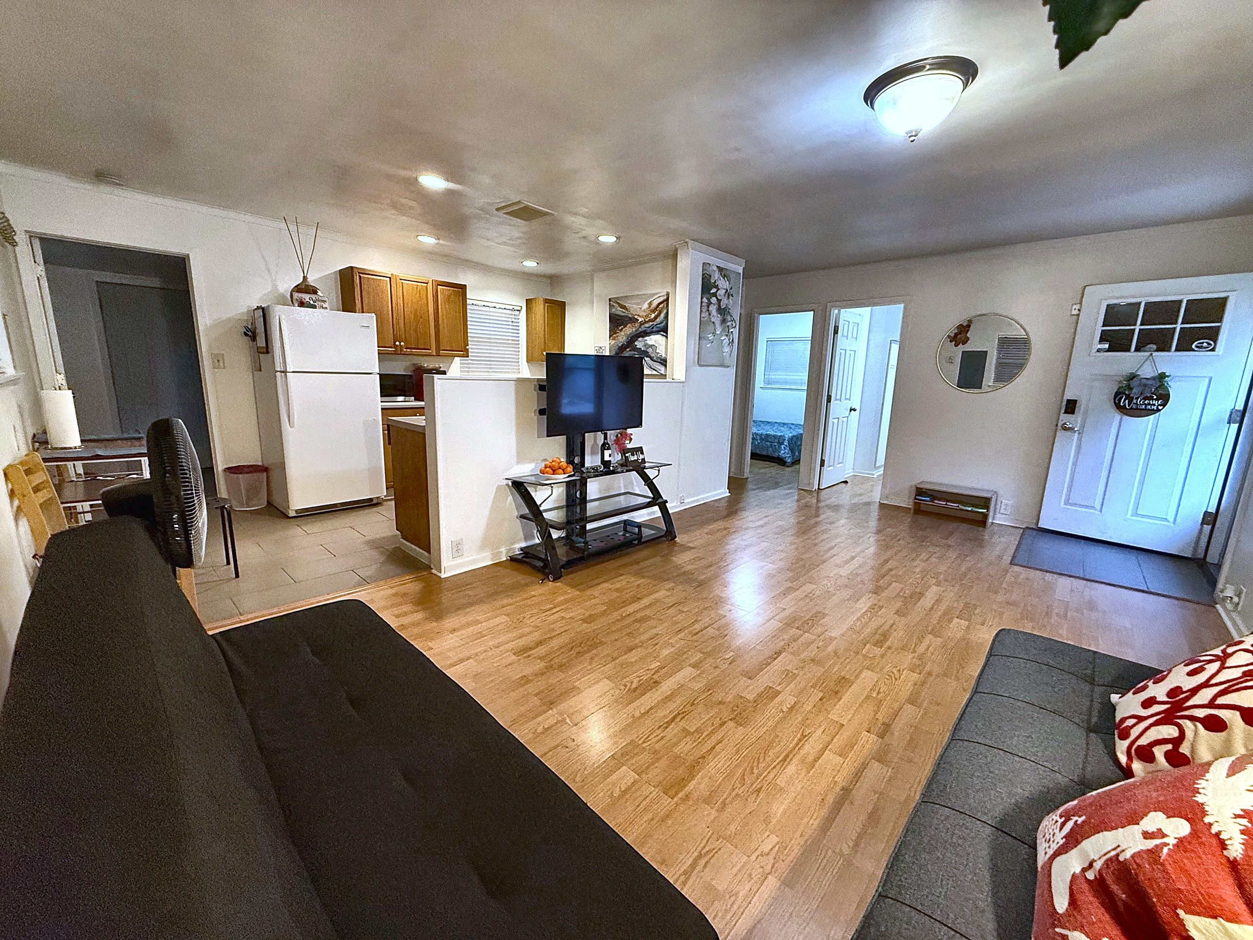 A compact living space with a kitchenette, a sofa, a dining area, and a door leading to another room.