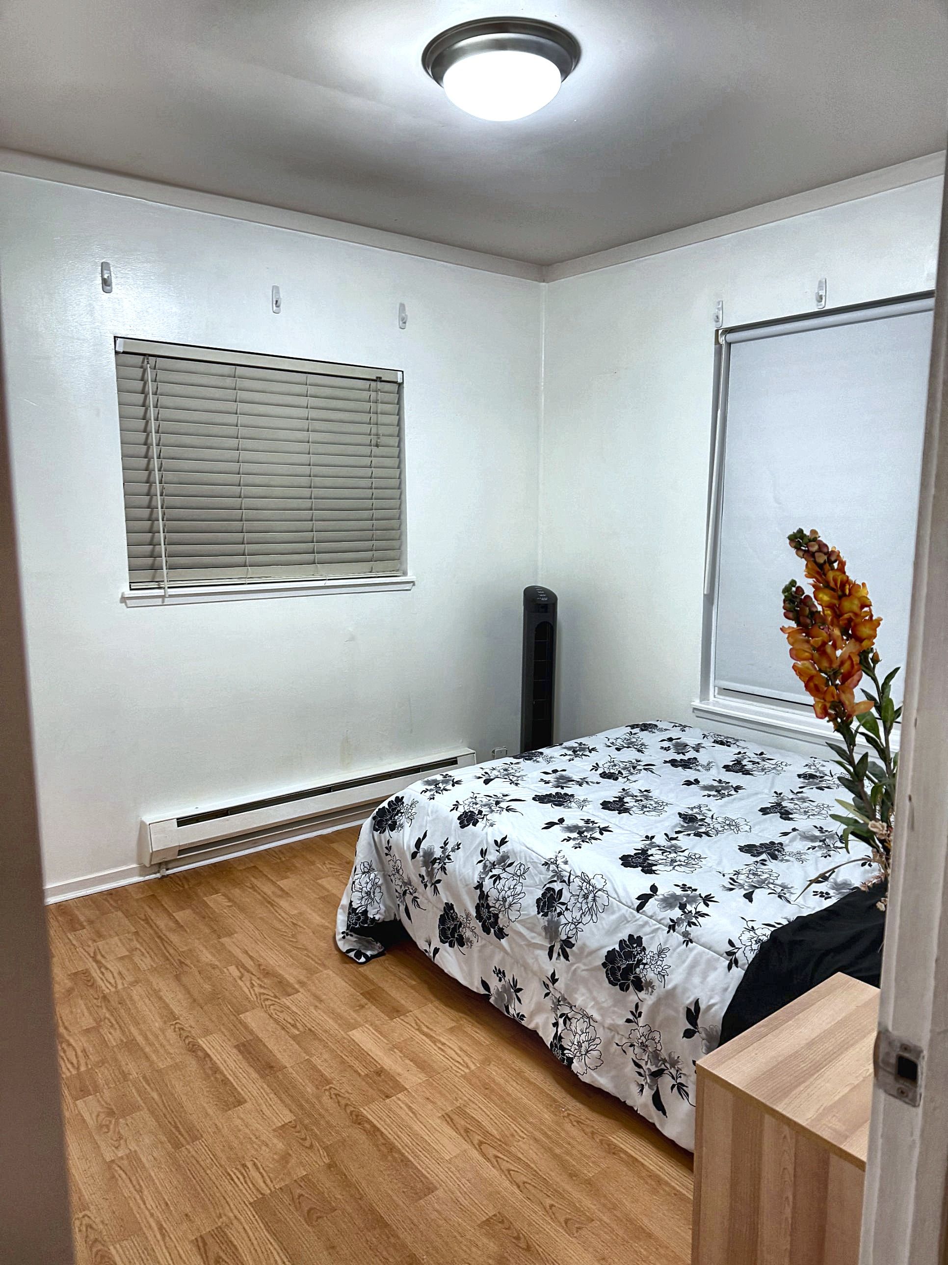 A bedroom with a bed, a window with blinds, a radiator, and a wooden floor.