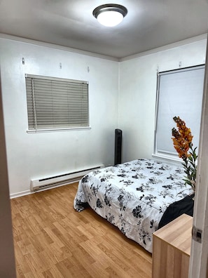 A bedroom with a bed, a window with blinds, a radiator, and a wooden floor.