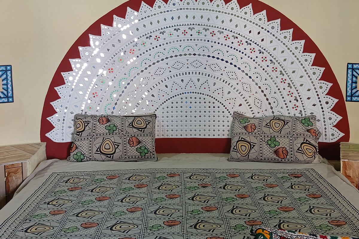 A room with a patterned bedspread, two pillows with intricate designs, and a decorative wall hanging with a radial pattern.
