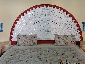 A room with a patterned bedspread, two pillows with intricate designs, and a decorative wall hanging with a radial pattern. - Raj Resort (Dholavira)