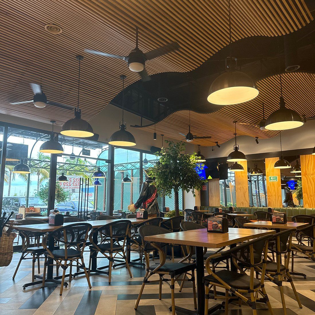 Un interior de restaurante con techos altos, paneles de madera y varias mesas y sillas para comer.