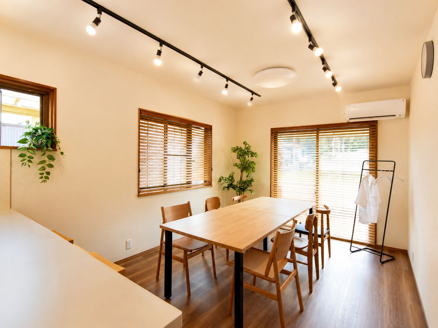 Una habitación con una mesa de madera, sillas, una planta y un perchero.