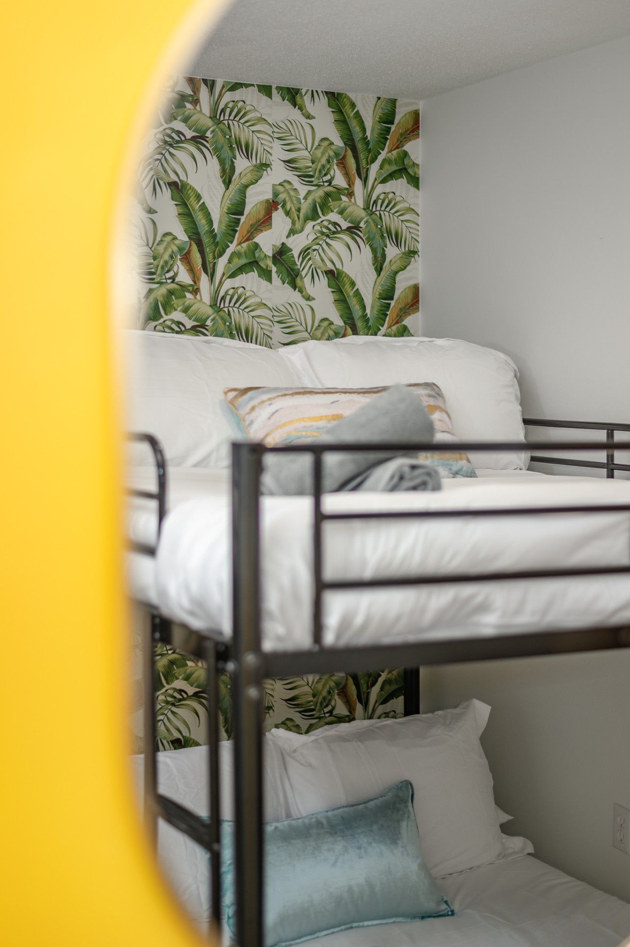 Ein Stockbett mit weißer Bettwäsche und einem tropischen Blattmuster an der Wand.