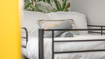 Ein Stockbett mit weißer Bettwäsche und einem tropischen Blattmuster an der Wand.