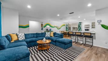 Een moderne woonkamer met een hoekbank, een ronde salontafel en een eetgedeelte met barkrukken.