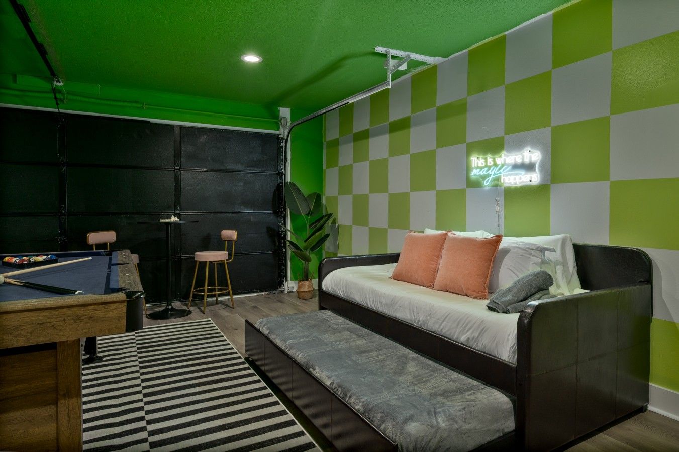Ein Zimmer mit Billardtisch, einem Bett mit Kissen, einer Bank und einer grünen Wand mit einem Neon-Schild.