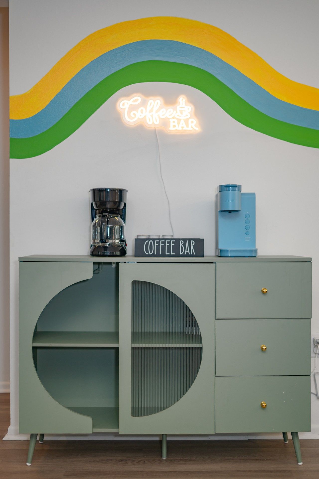 Ein Café-Aufbau mit einer Neonreklame, einer Kaffeemaschine und einem Wasserspender auf einem Türkis-farbenen Schrank.