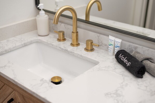 A bathroom sink with a gold faucet, a bottle of shampoo, and a towel labeled 'Makeup'.