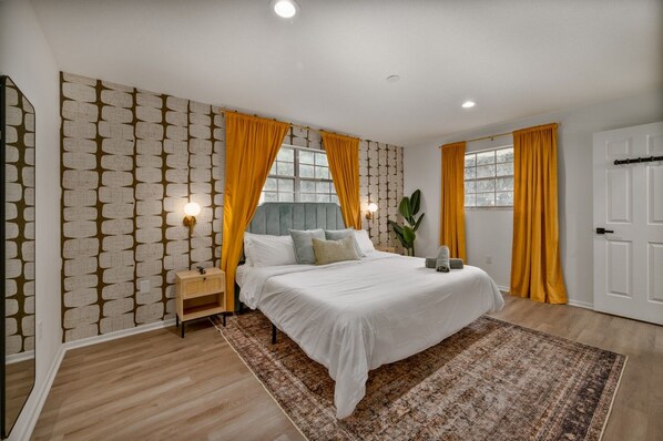A bedroom with a bed, nightstands, a window with curtains, a door, and a patterned wall.