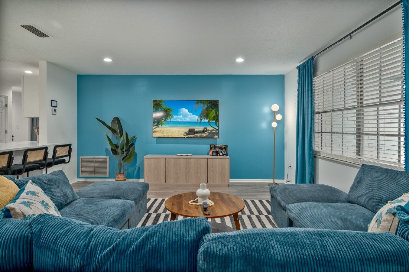 Ein Wohnzimmer mit blauer Wand, einem Flachbildfernseher, einem Essbereich mit Stühlen und einer großen Pflanze.