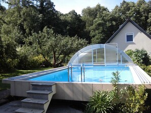 Ein Schwimmbad mit Glasüberdachung, umgeben von einem Garten und einem Haus.