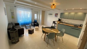 A modern living room with a sofa, coffee table, and ottoman, a dining area with a table and chairs, and a kitchen with cabinets and a sink. - New Listing (Saint-Vivien)