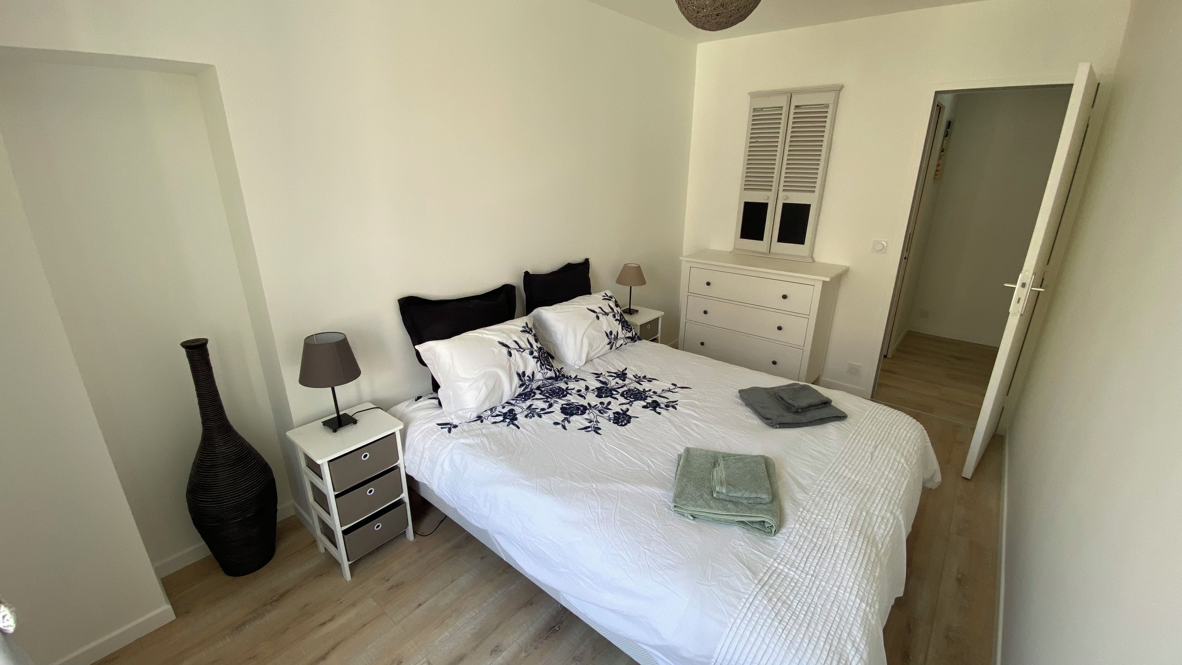 A bedroom with a bed, bedside tables, a dresser, a lamp, a vase, and a door.