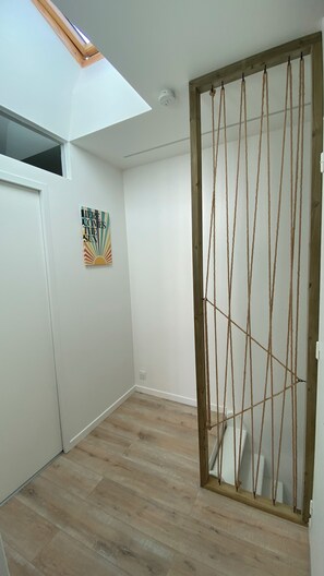 A room with a sloped ceiling, a wooden door with rope decorations, a small window, and a wall-mounted artwork. - New Listing (Saint-Vivien)