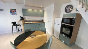 A compact kitchen with a dining area, a microwave, a refrigerator, and a clock on the wall. - New Listing (Saint-Vivien)