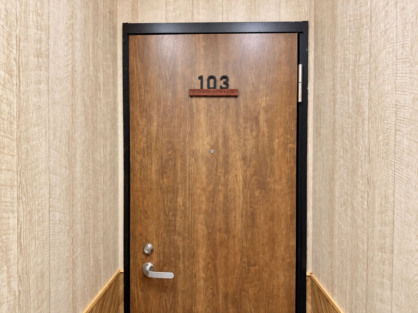 Een houten deur met het nummer 103 en een bord erboven.