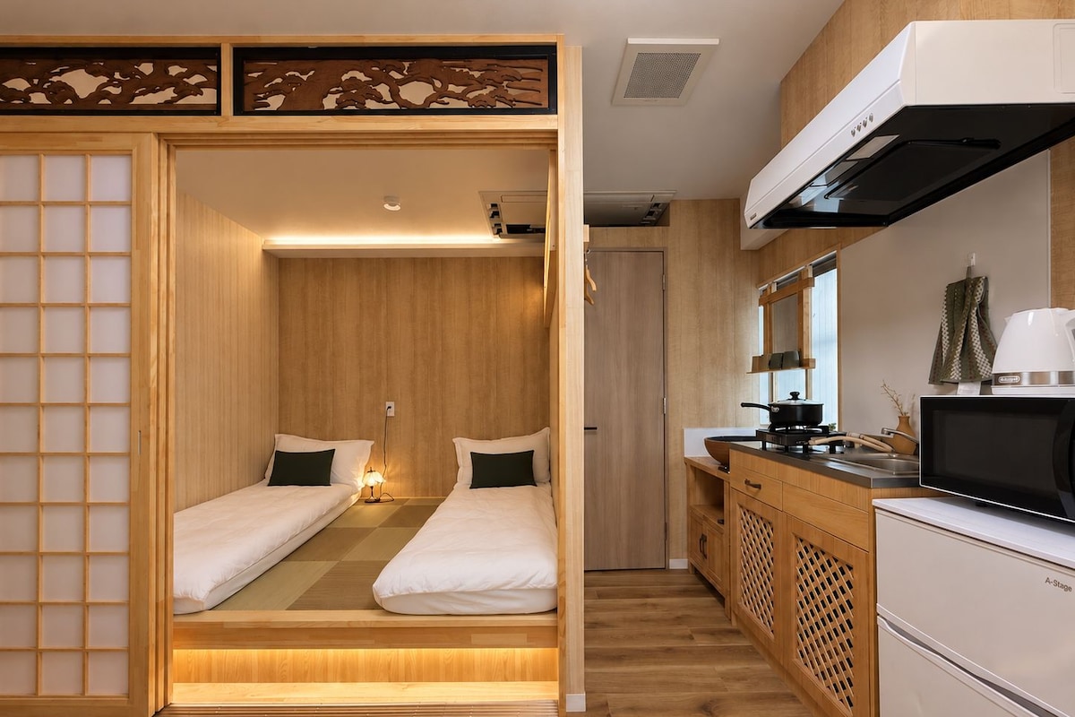 A compact room with two beds, a kitchenette, and a sliding door.
