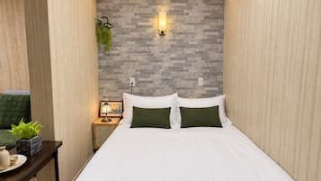 Een netjes opgemaakt bed met witte beddengoed en groene kussens, een nachtkastje met een lamp, en een wandlamp.