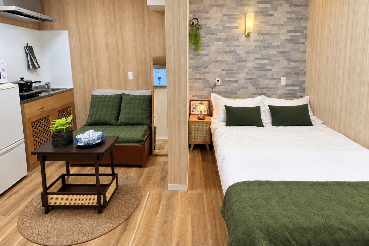 A compact room with a kitchenette, a sofa, a bed, and a small table.