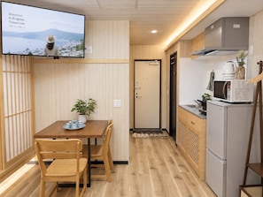 A compact kitchen with a dining area, a television mounted on the wall, and a view of a mountainous landscape. - TOKYO MOON HOUSE - Skytree Rooftop (Sumida City)