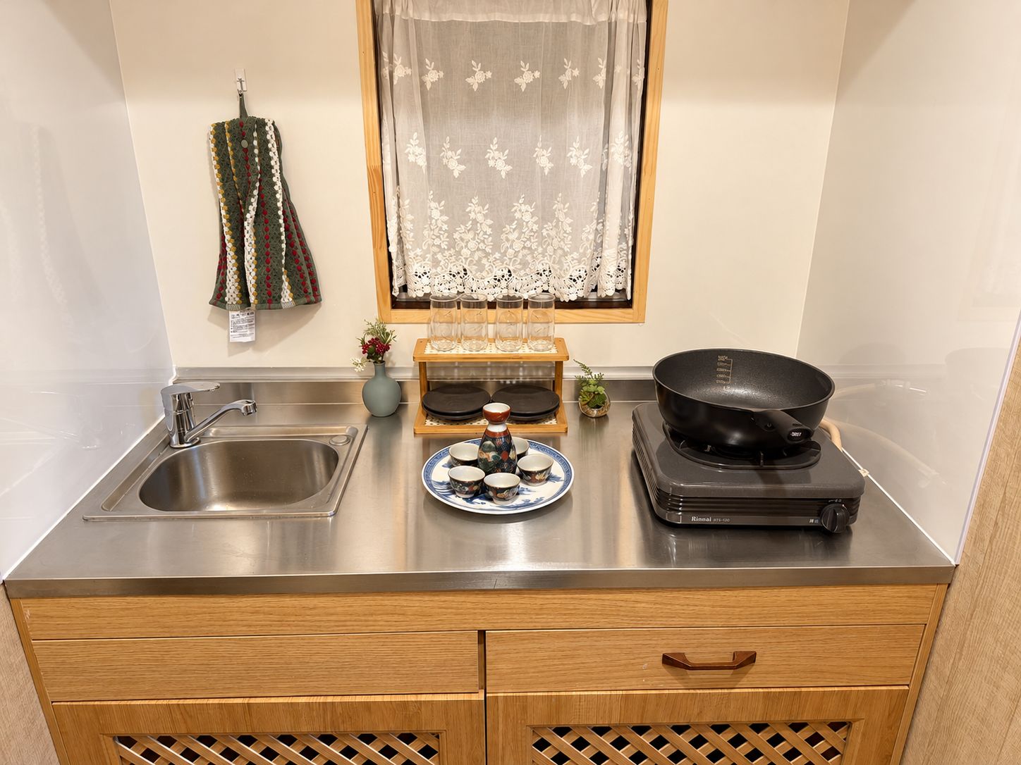 Een keuken met een roestvrijstalen spoelbak, houten kastjes, een Rinnai inductiekookplaat en een kantelaar.
