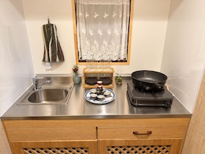 Cuina amb un rentaplatets d'acer inoxidable, armaris de fusta, fogó per inducció Rinnai i un detall de vesta a la finestra.