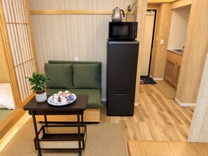 A compact living space with a sofa, a small table with a tray of dishes, a microwave, and a refrigerator. - TOKYO MOON HOUSE - Skytree Rooftop (Sumida City)