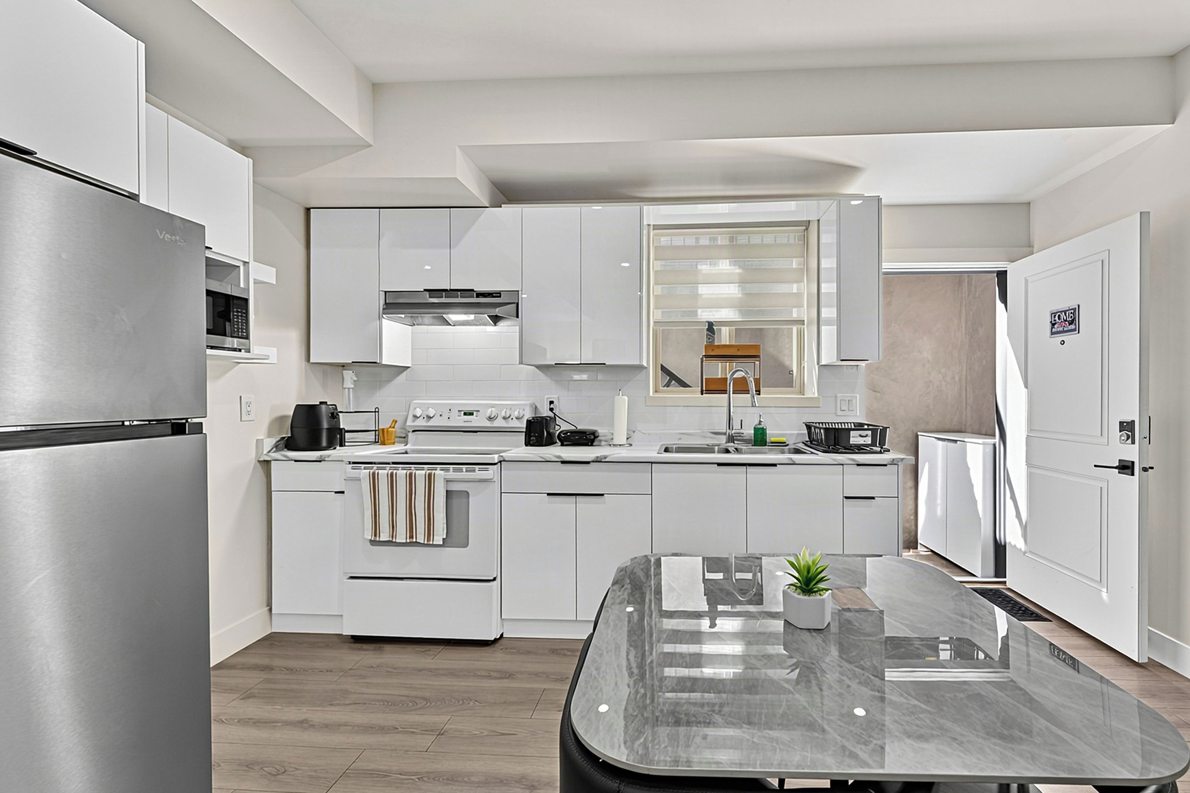 Eine moderne Küche mit weißen Schränken, einem Edelstahl-Kühlschrank, einem eingebauten Backofen und einer zentralen Kochinsel mit Marmorarbeitsplatte.