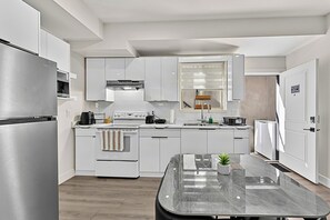 A modern kitchen with white cabinetry, a stainless steel refrigerator, a built-in oven, and a central island with a marble countertop. - Cozy private basemen suite in surrey (Surrey)