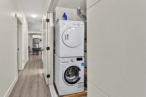 A laundry room with stacked washers and dryers, a wooden floor, and a hallway leading to a dining area. - Cozy private basemen suite in surrey (Surrey)