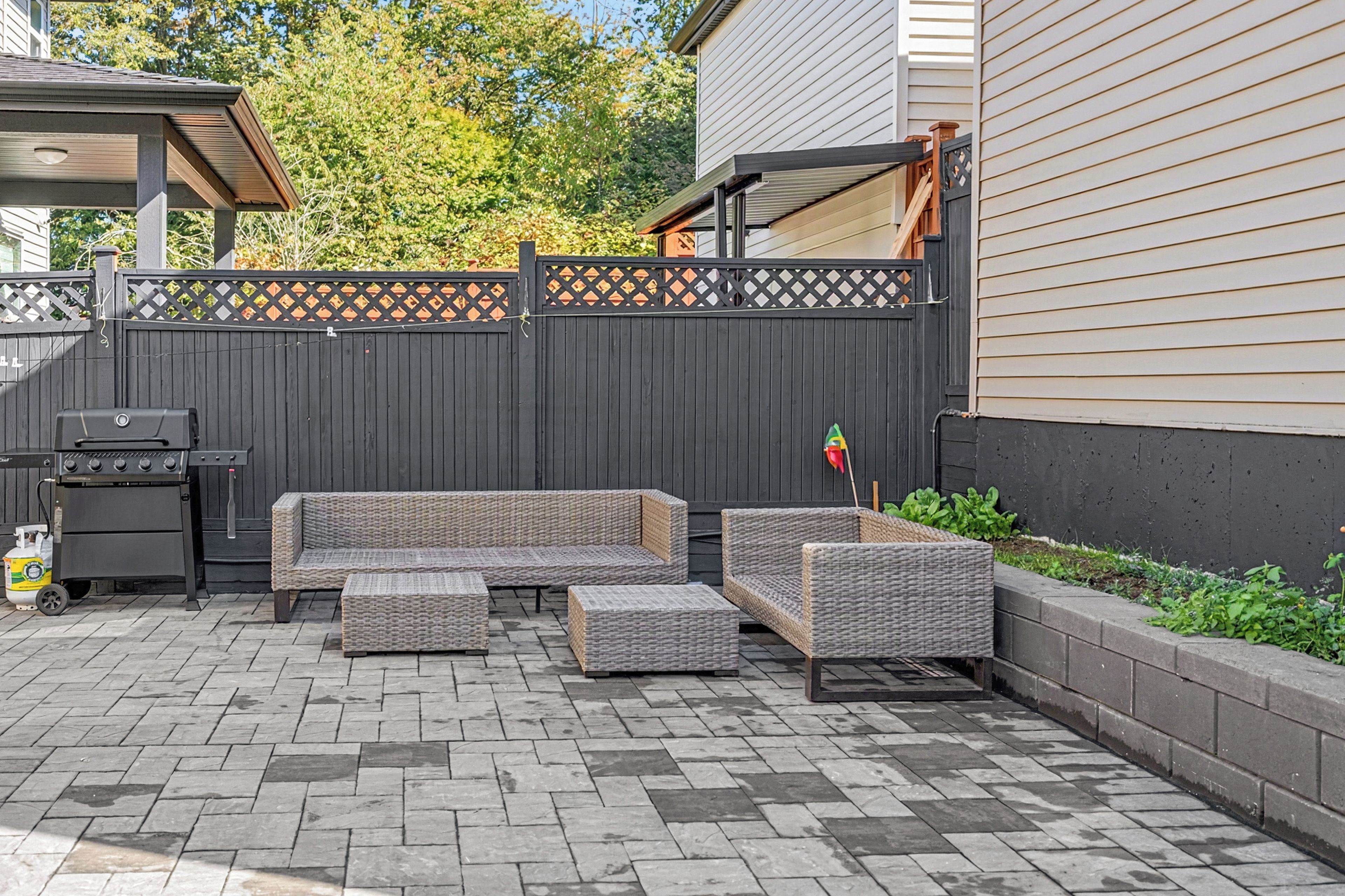 Eine Terrasse mit Grill, Korbmöbeln und einem Holzzaun.