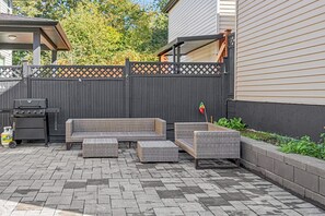 A patio with a grill, wicker furniture, and a wooden fence. - Cozy private basemen suite in surrey (Surrey)