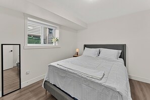Quarto com cama, janela, mesa de cabeceira e espelho.