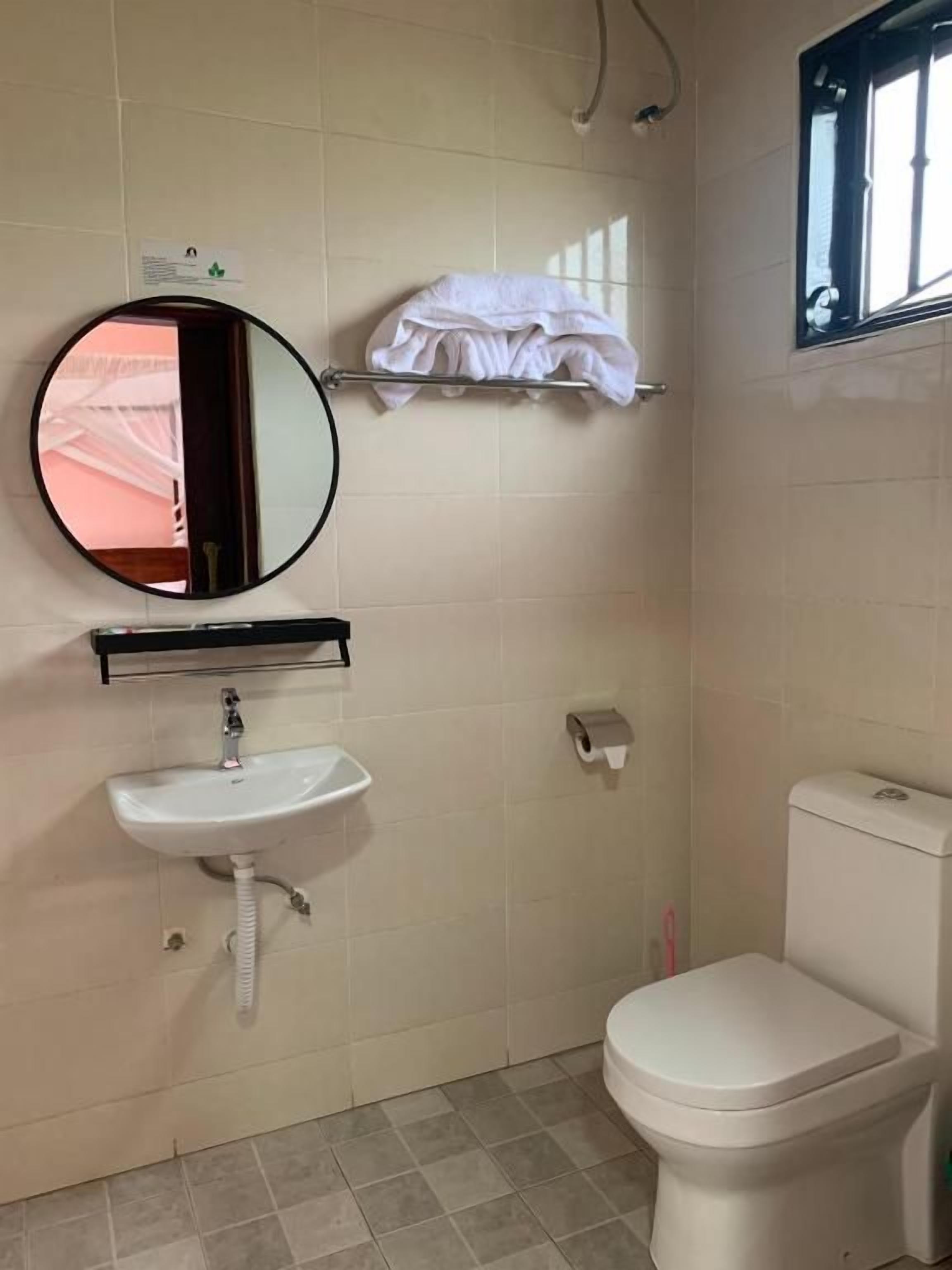 Un baño con espejo redondo, lavamanos, inodoro y toallero.