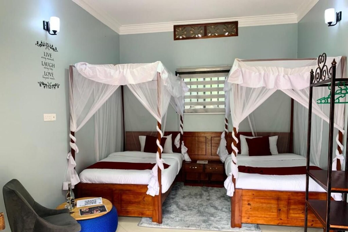 A room with two beds, each with a canopy, a small round table, a chair, and a wall with a motivational quote.