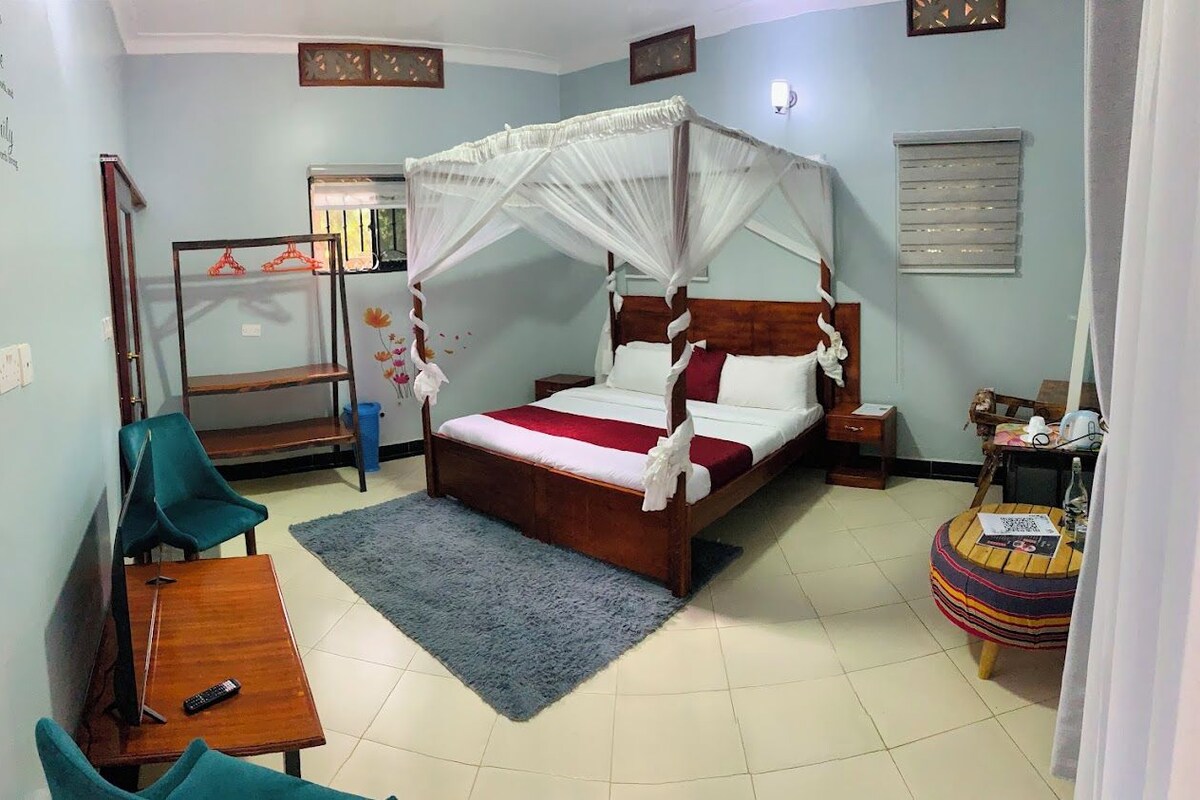 A bedroom with a four-poster bed, a small round table, a desk with a chair, and a mirror.