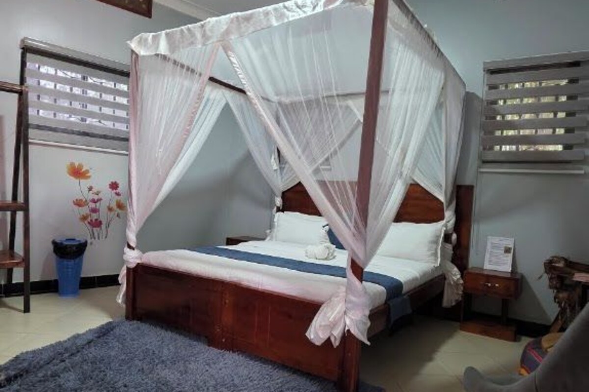 A room with a four-poster bed, a blue rug, and a chair.