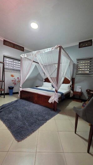 A room with a four-poster bed, a blue rug, and a chair. - Nkokonjeru White Cove Mbarara (Mbarara)