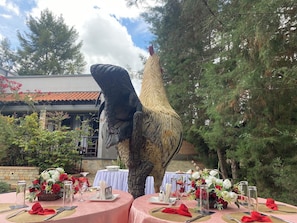 An outdoor dining area with tables set for a meal, surrounded by trees and a large bird sculpture. - Nkokonjeru White Cove Mbarara (Mbarara)